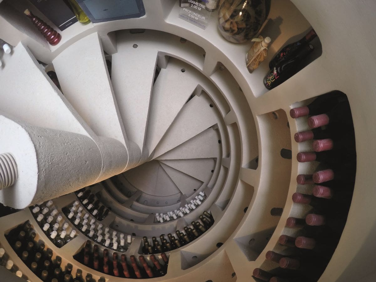 Cave à vin maison ronde avec escalier hélicoïdal blanc et remplie de bouteilles de vin.